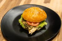 Pesto Chicken Sandwich with Parmesan Pesto Chicken Sandwich with Parmesan on a sesame bun with tomato and lettuce, on a black plate.