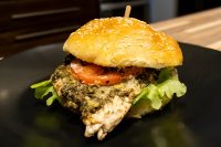 Pesto Chicken Sandwich with Parmesan Pesto Chicken Sandwich with Parmesan on a sesame bun with tomato and lettuce, skewered on a dark plate.