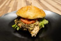 Pesto Chicken Sandwich with Parmesan Pesto Chicken Sandwich with Parmesan on a sesame bun with tomato and lettuce, on a black plate.