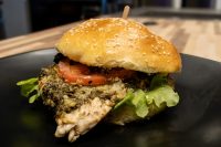 Pesto Chicken Sandwich with Parmesan Pesto Chicken Sandwich with Parmesan on a sesame bun with tomato and arugula, on a dark plate.