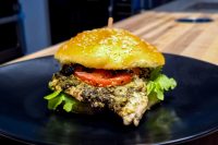 Pesto Chicken Sandwich with Parmesan Pesto Chicken Sandwich with Parmesan on a sesame bun with tomato and lettuce, served on a black plate.