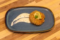 Breaded Tuna Cake topped with lemon slice and parsley, served with creamy sauce on a blue plate