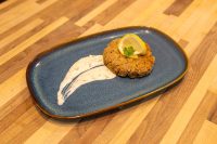 Golden breaded Tuna Cake topped with a lemon slice and herb sprig, served with a creamy sauce swoosh.