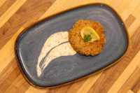 Golden Tuna Cakes patty topped with lemon and herb, served with creamy sauce on a blue plate.