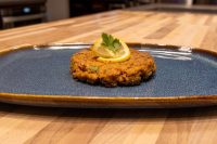 A browned Tuna Cake topped with a lemon slice and parsley on a dark blue plate.