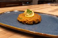 A golden-brown Tuna Cake topped with a lemon slice and parsley sprig on a blue ceramic plate.
