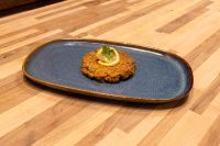 A fried Tuna Cake topped with a lemon slice and herb garnish, served on a blue oval plate.