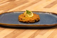 A fried Tuna Cake on a dark blue plate, garnished with a lemon slice and parsley sprig.