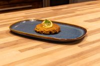 Golden fried Tuna Cake topped with a lemon slice and herb sprig on a blue oval plate.
