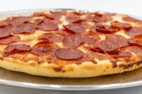 60 min. Pan Pizza Close-up of 60 min. Pan Pizza with thick crust and overlapping pepperoni slices on a metal tray.