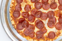 60 min. Pan Pizza Overhead close-up of baked 60 min. Pan Pizza topped with pepperoni and melted cheese in a metal pan.