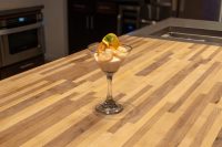 A stemmed glass of Shrimp Cocktail with creamy sauce and a citrus garnish on a wooden countertop.