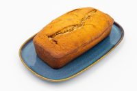 A golden-brown loaf of Banana Bread with a split top crust, on a blue oval plate.