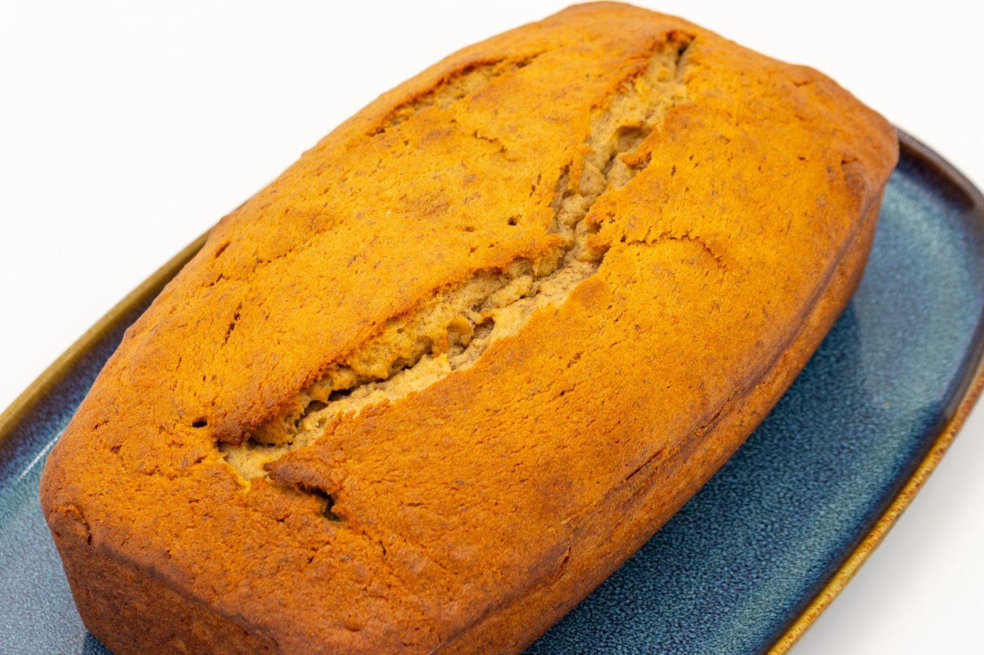 Golden-brown Banana Bread loaf with a cracked top, resting on a dark blue plate.