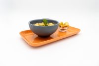 Bowl of creamy Czech Garlic Soup Cesnecka garnished with herbs, served on an orange tray with roasted potatoes.