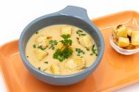 Bowl of creamy Czech Garlic Soup Česnečka with croutons, parsley, and chives on an orange tray