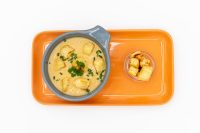 Bowl of Czech Garlic Soup Cesnecka with croutons and herbs on an orange tray beside a jar of croutons.
