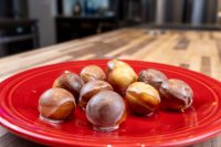 Glazed Donut Holes piled on a red ceramic plate on a wooden countertop.