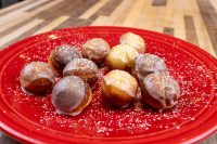 Donuts and Donut Holes Glazed Donuts and Donut Holes dusted with powdered sugar, arranged on a red plate.