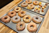 Donuts and Donut Holes Two trays of glazed Donuts and Donut Holes, some topped with sprinkles, on a wooden counter