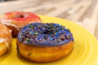 Purple-glazed Donuts and Donut Holes topped with colourful sprinkles on a yellow plate.