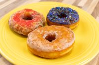 Three glazed Donuts and Donut Holes on a yellow plate: red sugar, blue with sprinkles, and golden glaze.