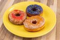 Donuts and Donut Holes Three glazed donuts on a yellow plate, one with red sprinkles, one with dark sprinkles, one plain.