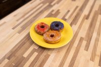 Three glazed Donuts with red, blue-sprinkled, and plain glaze on a yellow plate on a wood table