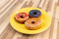 Donuts and Donut Holes Three glazed Donuts and Donut Holes—orange, blue with sprinkles, and plain—on a yellow plate.