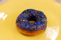 Donuts and Donut Holes A single Donuts and Donut Holes ring with purple glaze and colorful sprinkles on a yellow plate.