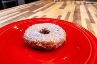 Donuts and Donut Holes A glazed doughnut from Donuts and Donut Holes, topped with white sprinkles, on a red plate.