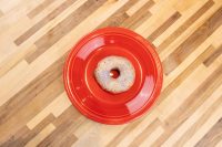Donuts and Donut Holes A single glazed donut with a sugary textured coating centered on a red plate atop a wood-plank table.