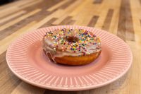 A single glazed Donuts and Donut Holes ring topped with rainbow sprinkles on a pink ridged plate