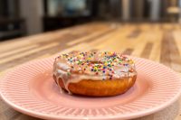 Donuts and Donut Holes Glazed Donuts and Donut Holes with rainbow sprinkles and drips of glaze on a pink ridged plate