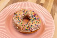 Donuts and Donut Holes A glazed donut from the Donuts and Donut Holes recipe, covered in colorful sprinkles, on a pink plate.