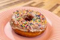 Donuts and Donut Holes A ring-shaped Donuts and Donut Holes pastry with white glaze and rainbow sprinkles on a pink plate