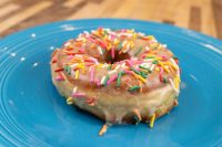 Donuts and Donut Holes A glazed ring donut from Donuts and Donut Holes topped with rainbow sprinkles on a blue plate.