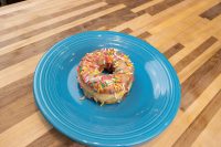 Donuts and Donut Holes A glazed Donuts and Donut Holes topped with rainbow sprinkles on a blue plate atop a wooden table.
