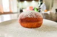 Czech Filled Donuts Koblihy A powdered-sugar-dusted Czech Donuts Koblihy on a white plate with sugar scattered around it.