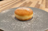 Czech Filled Donuts Koblihy A single fried Czech Filled Donuts Koblihy dusted with powdered sugar on a grey plate.