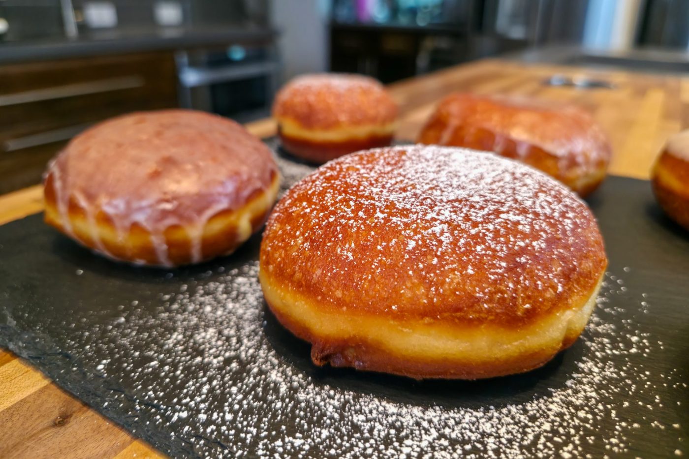 Czech Filled Donuts Koblihy Powdered sugar dusted and glazed Czech Filled Donuts Koblihy on a dark slate board.