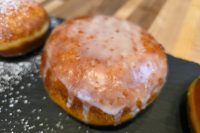 Glazed Czech Filled Donuts Koblihy on a dark slate board with powdered sugar scattered nearby.