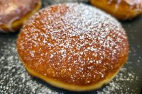 Czech Filled Donuts Koblihy Close-up of a Czech Filled Donuts Koblihy dusted with powdered sugar, more donuts blurred behind it.