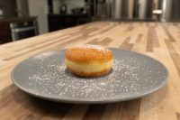 A single Czech Filled Donuts Koblihy dusted with powdered sugar on a grey plate on a wooden table.
