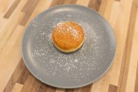 Czech Filled Donuts Koblihy A single golden Czech Filled Donuts Koblihy dusted with powdered sugar on a gray plate.