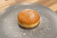 Czech Filled Donuts Koblihy A single Czech Filled Donuts Koblihy with a glossy top dusted in powdered sugar on a grey plate.