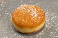 A whole Czech Donuts Koblihy, golden-fried and dusted with powdered sugar, resting on a gray plate.