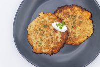 Potato Pancakes Bramboraky Two crispy Potato Pancakes Bramboraky on a dark plate topped with sour cream and chopped herbs.