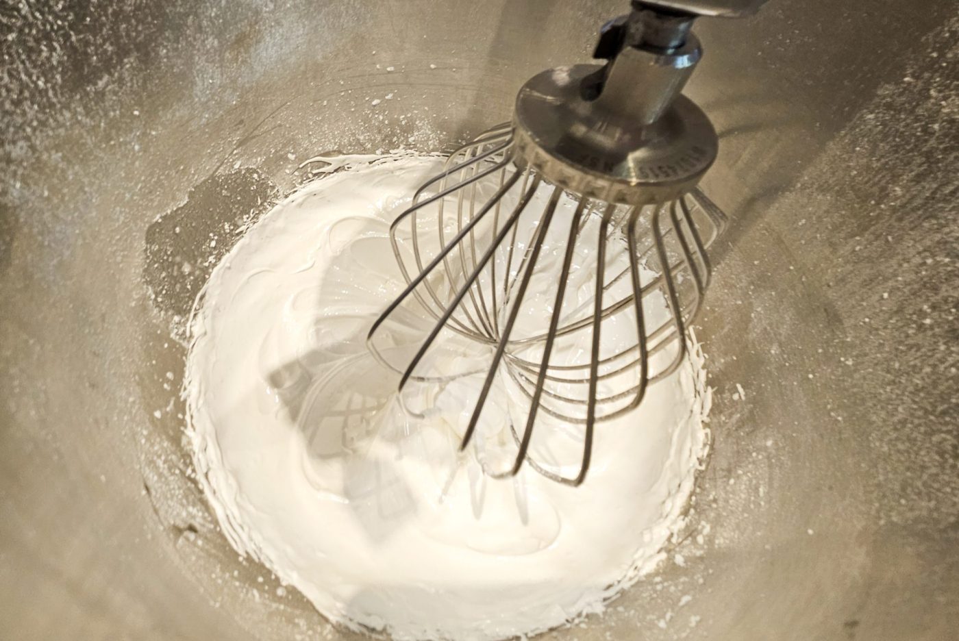 Wire whisk attachment mixing fine white powder in a metal bowl, part of preparing Gingerbread Heart Cookies icing.
