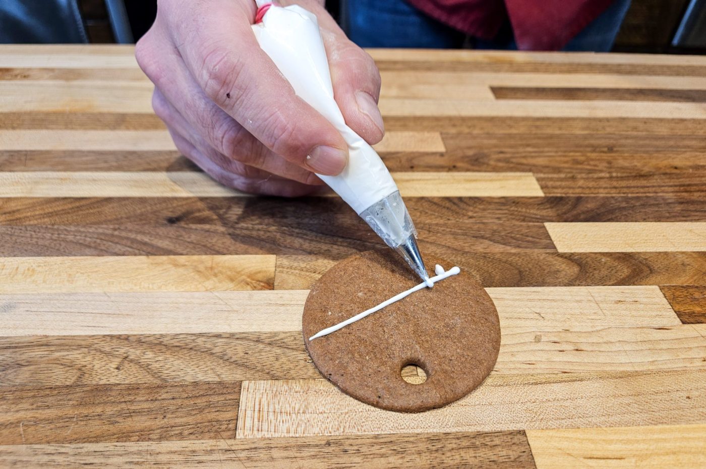 Hand piping white icing across a round gingerbread cookie on a wooden table